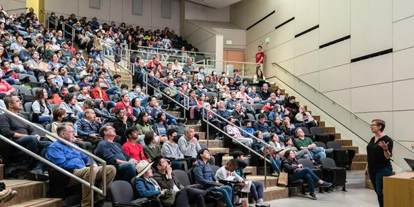 presenter stands in front of audience inside auditorium