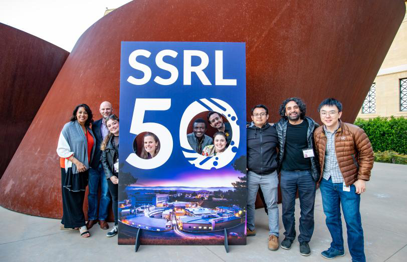 Participants pose in front of poster for SSRL's 50th Anniversary event